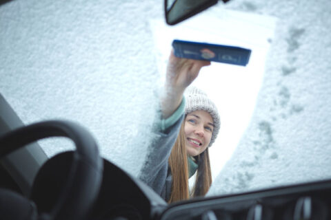 一个女孩擦拭车雪覆盖的汽车挡风玻璃